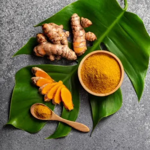 Turmeric powder and fresh turmeric root on grey concrete background with copyspace. Spice, natural coloring, alternative medicine.